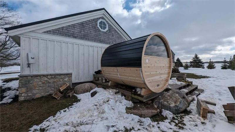 Cedar barrel sauna with a dark roof beside a home