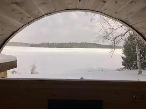 A winter lake view through a sauna’s half-moon window
